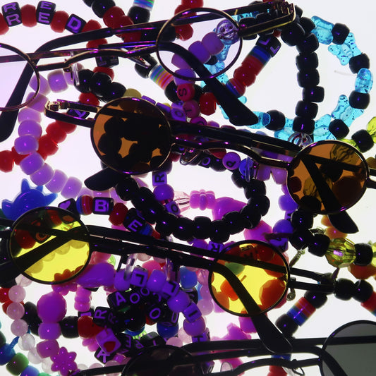 A pile of eyeglasses with colorful beaded straps, including red, blue, purple, yellow, and black beads, on a plain white background.