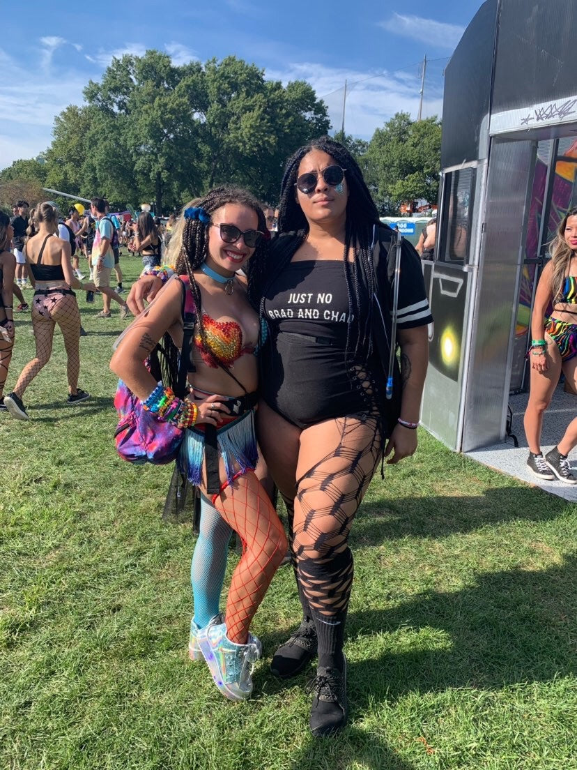 Two people posing together at a music festival with a grassy area and festival attendees in the background.