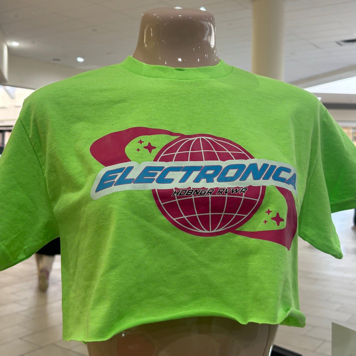Green crop t-shirt with a logo on a hanger against a tiled wall background