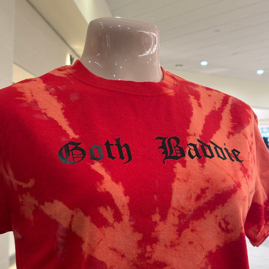 Red tie-dye shirt with 'Goth Baddie' text on a hanger against a white wall.