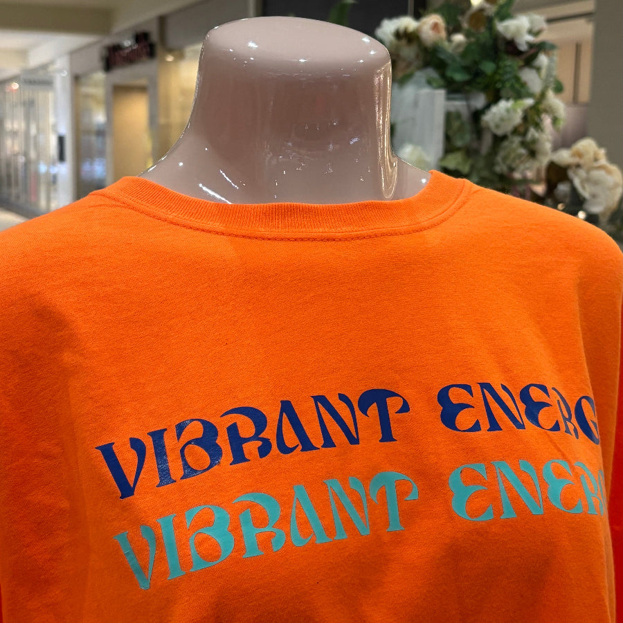 Orange sweatshirt with 'Vibrant Energy' text on a mannequin in an indoor setting.
