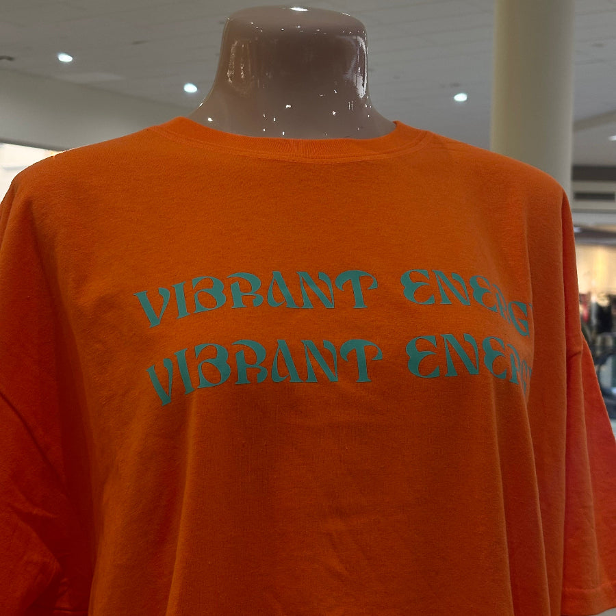 Orange t-shirt with 'Vibrant Energy' text on a mannequin in a store setting