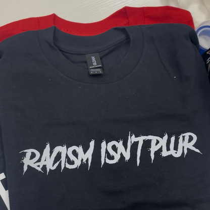 A folded black t-shirt with a red collar band, featuring the text 'RACISM ISN'T PLUR' printed in a stylized white font across the chest.