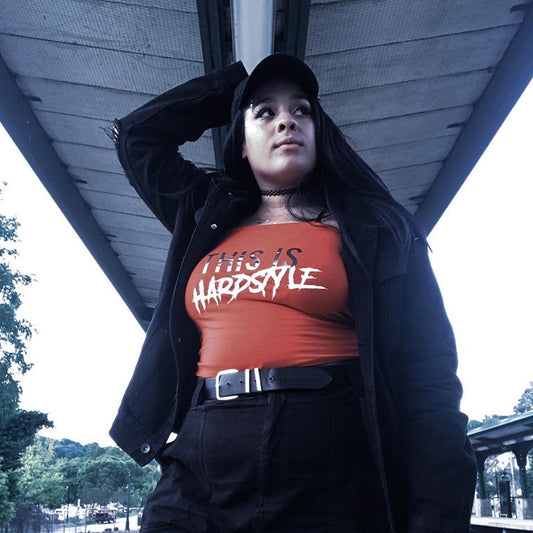 Girl on a train platform with a red tube top that says "This is Hardstyle." 